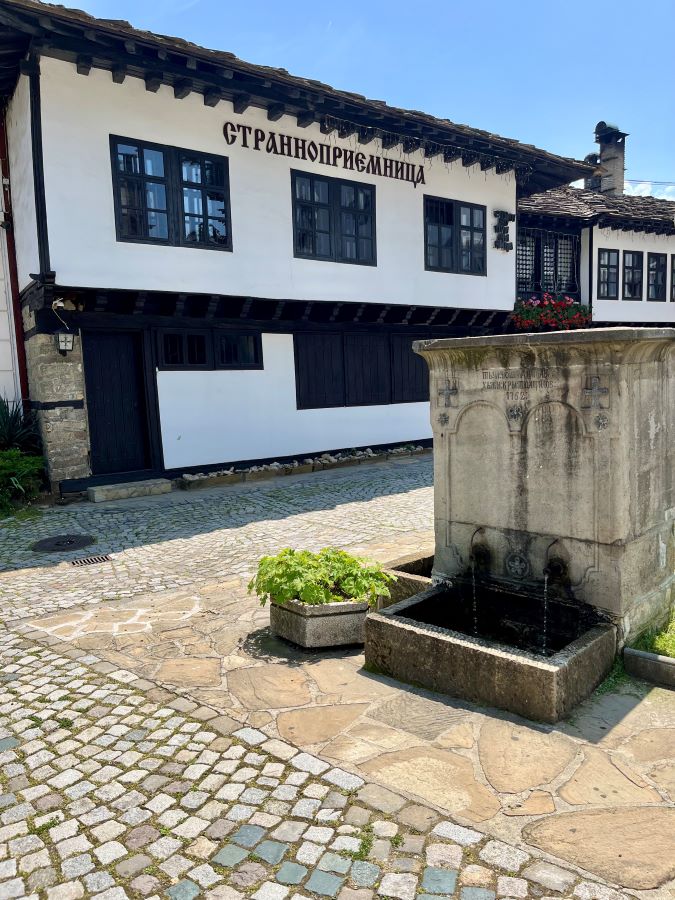 Каменна градска чешма с два чучура, издялан надпис „1762“ и кръстове върху каменния фронтон, заснета на калдъръмен площад в старинен градски център.