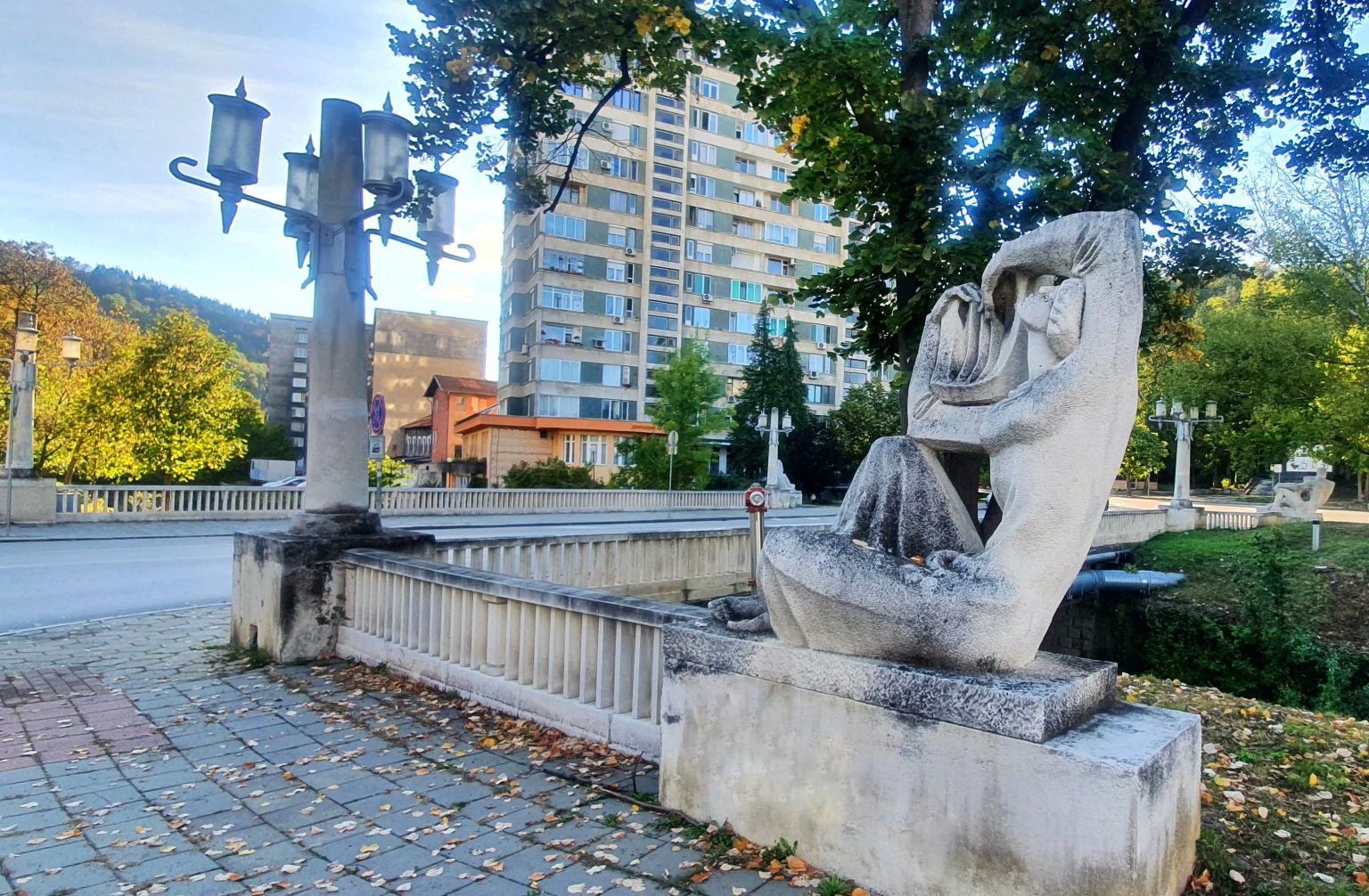 Снимка на Боровския мост („Мост на изкуствата“) в Габрово – градски мост с каменна балюстрада и бяла скулптурна фигура до реката, близо до Дома на културата и Летния театър.