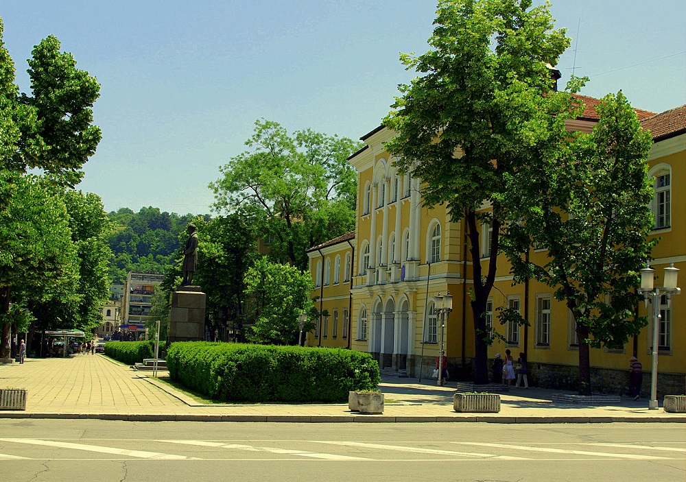 Сграда на Национална Априловска гимназия и паметник на Васил Априлов в центъра на Габрово, градска снимка с дървета и пешеходна зона