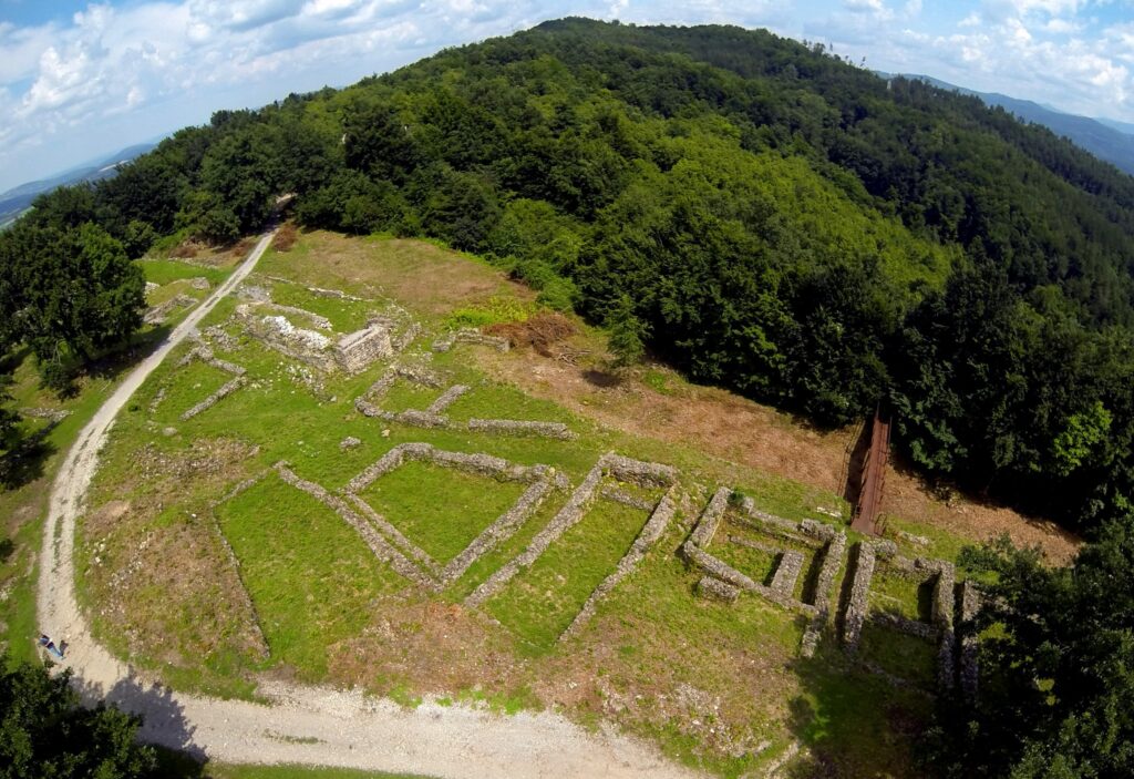 Въздушна снимка на разкритите зидове и план на крепост „Градище“ сред горист хълм – историческа забележителност в България.