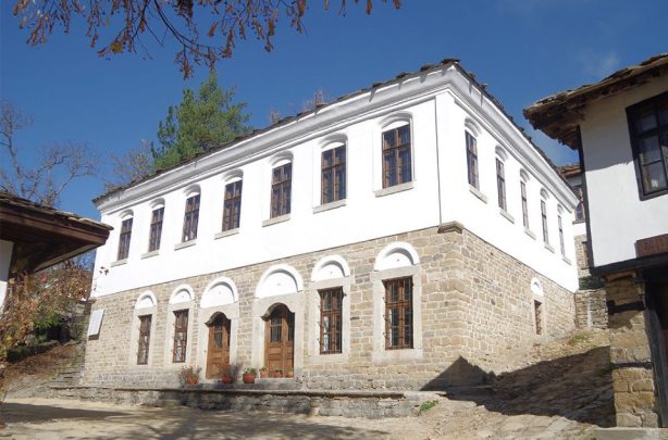 Бяла възрожденска сграда с каменна основа и дървени прозорци в МАИР Боженци